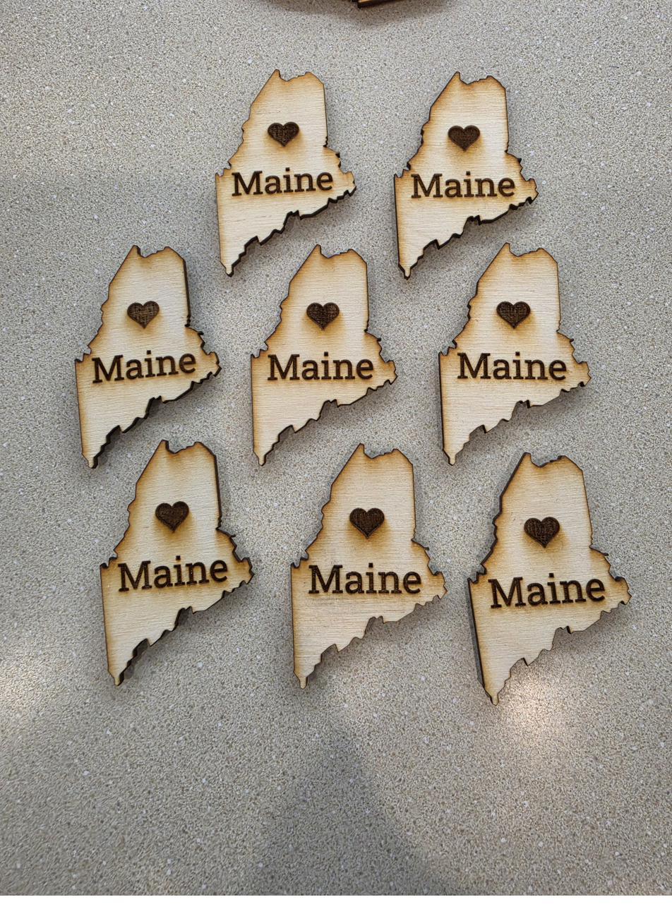 Laser-cut wooden ornaments shaped like the state of Maine, each with a heart burned into it.